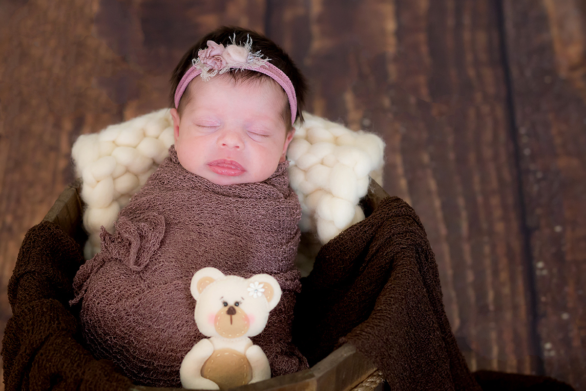 Ensaio de Newborn em Pará de Minas no baldinho, prop. Pose newborn enrolado no wrap com ursionho. Piso em madeira.