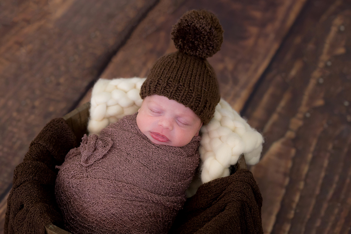 Ensaio newborn com touca em Pará de Minas. Posicionado no prop e piso de maderia.