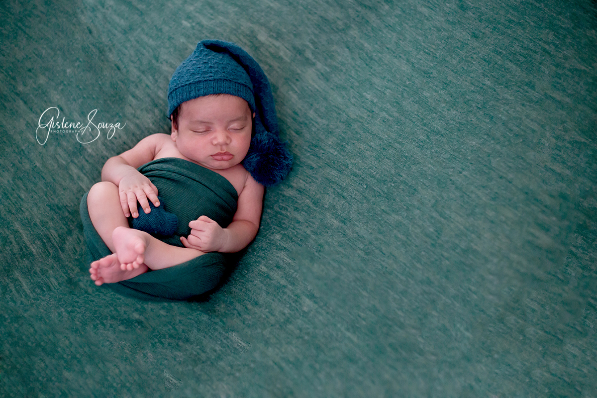 Fotografia, ensaio de newborn na cidade de Belo Horizonte. Bebê no puff enrolado no wrap. Composição em tons de verde.