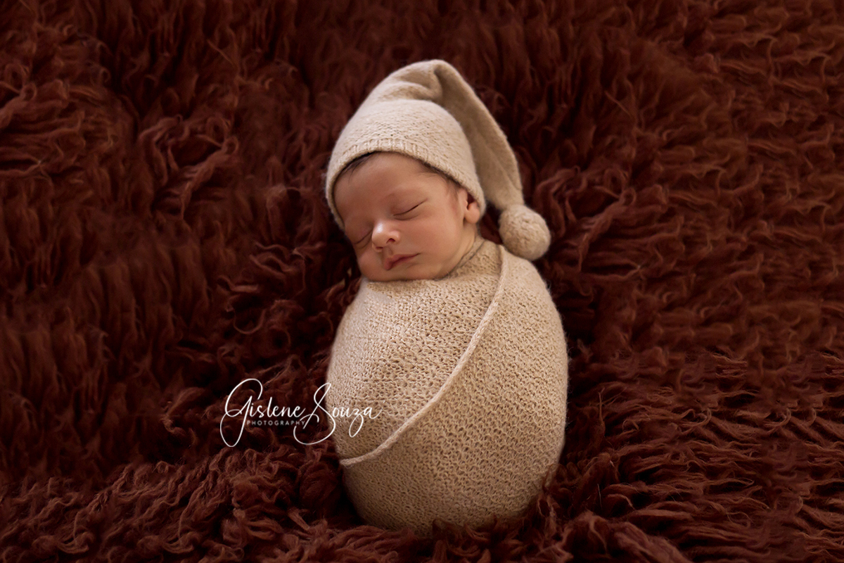 Fotografia de newborn. Bebê enrolado no wrap sobre o pelo. Wrap e touca Newborn Shop Brasil.