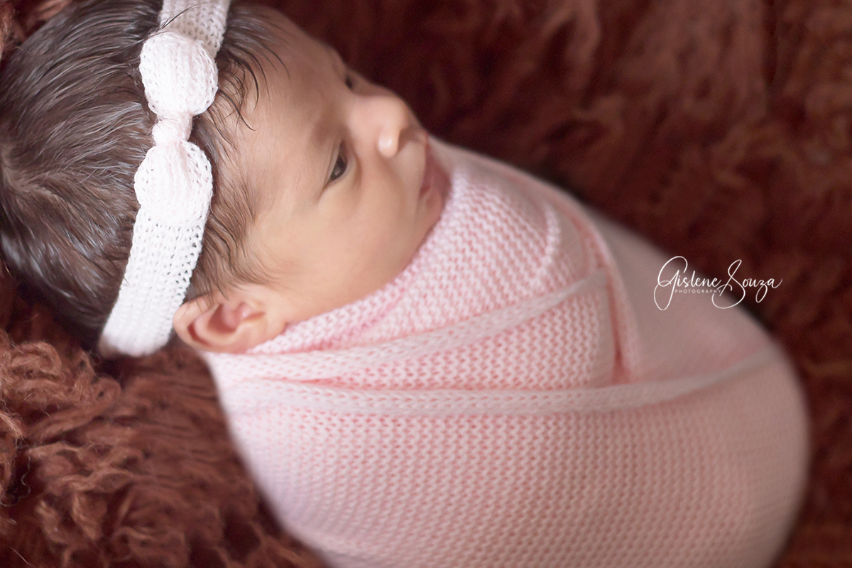 Ensaio de recém nascido, newborn no pelo. Menina pose enrolada no wrap. Composição contrastante de marrom com rosa bebê.