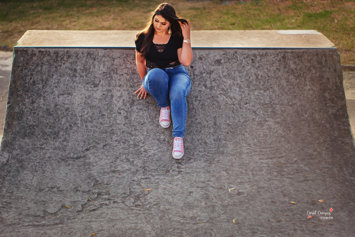 Fotografia de menina sentada na rampa de pista de skate, olhando para baixo e mexendo no cabelo em ensaio realizado em Caçapava do Sul RS