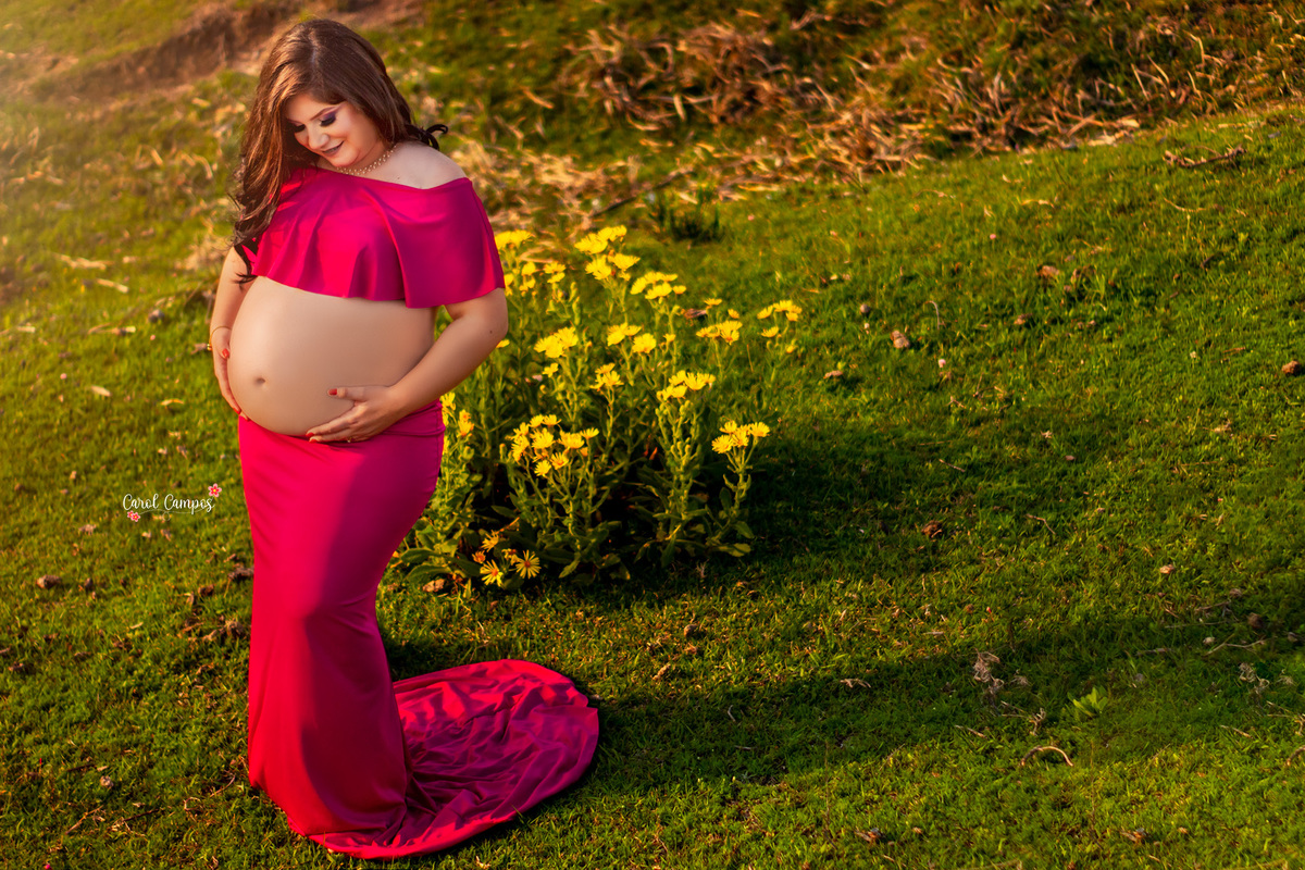 Fotografia da gestante com vestido rosa, olhando para a barriga e com as mãos na barriga.