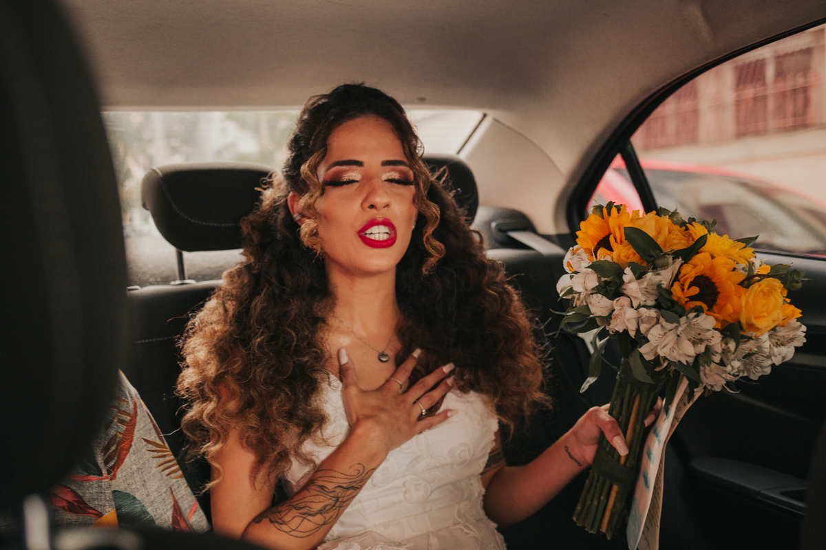 noiva a caminha da cerimonia fazendo sua oração com buque de flores amarelas e batom vermelho