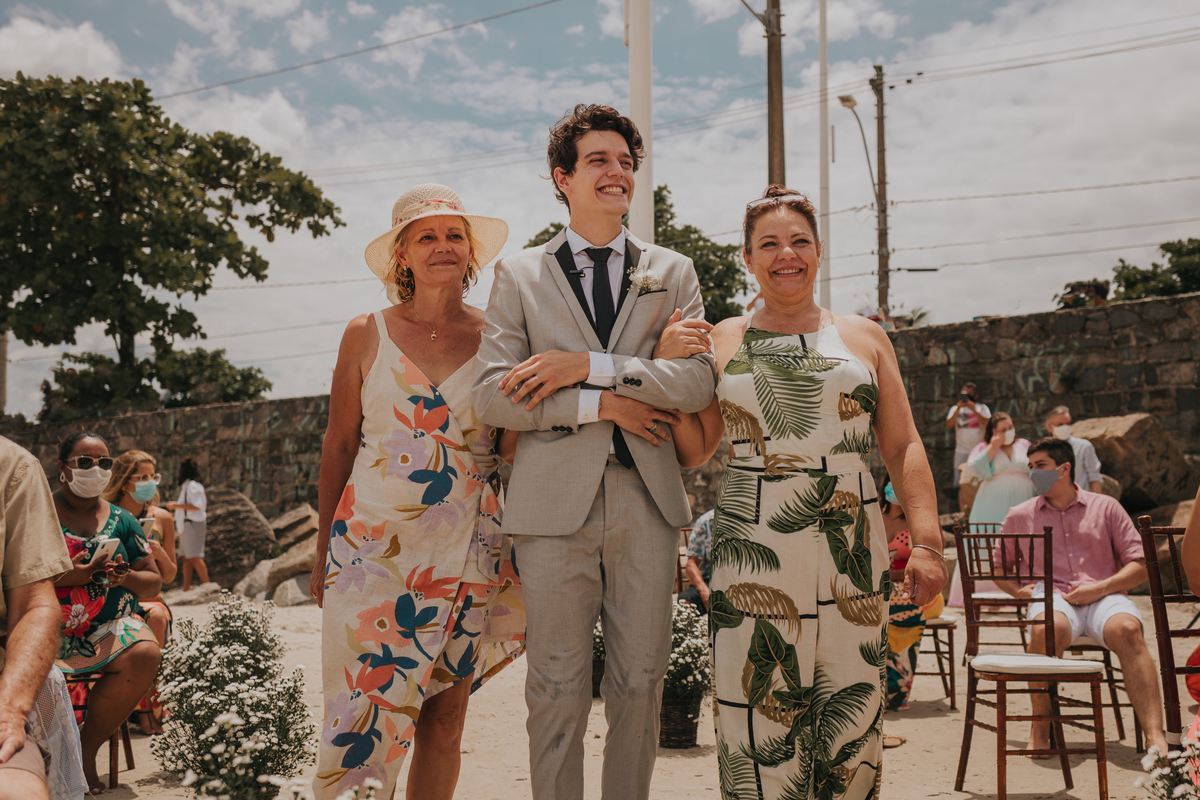 noivo com as duas mães entrando em cerimonia na praia de são vicente.
