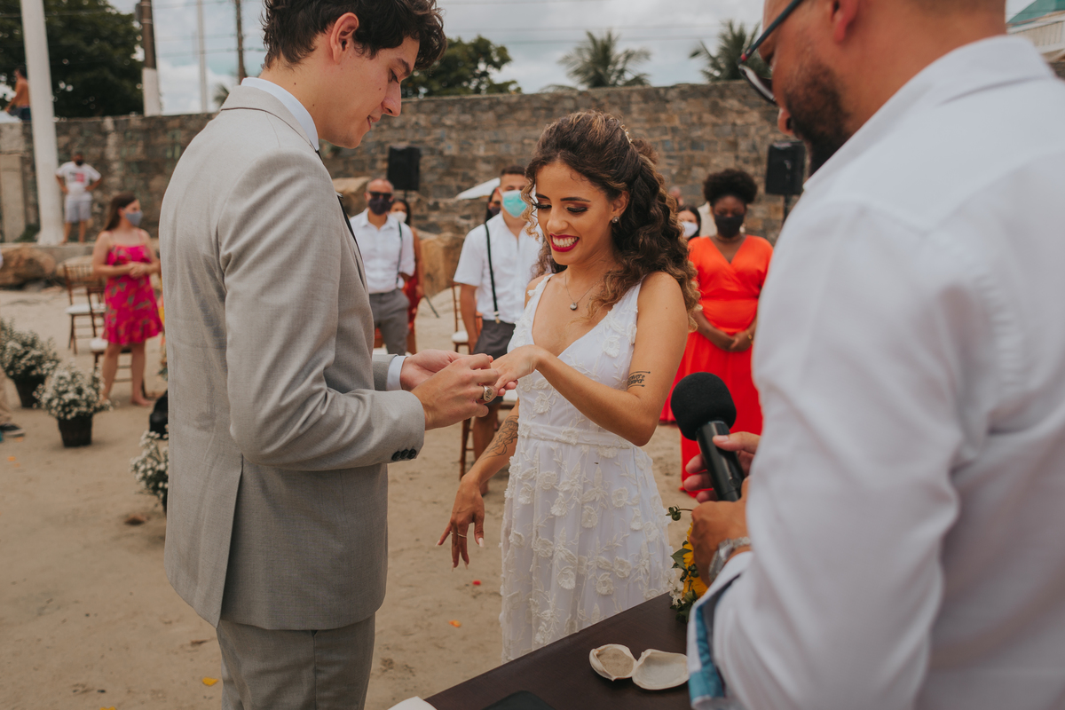 noivo colocando a aliança na noiva em casamento de dia na praia de são vicente