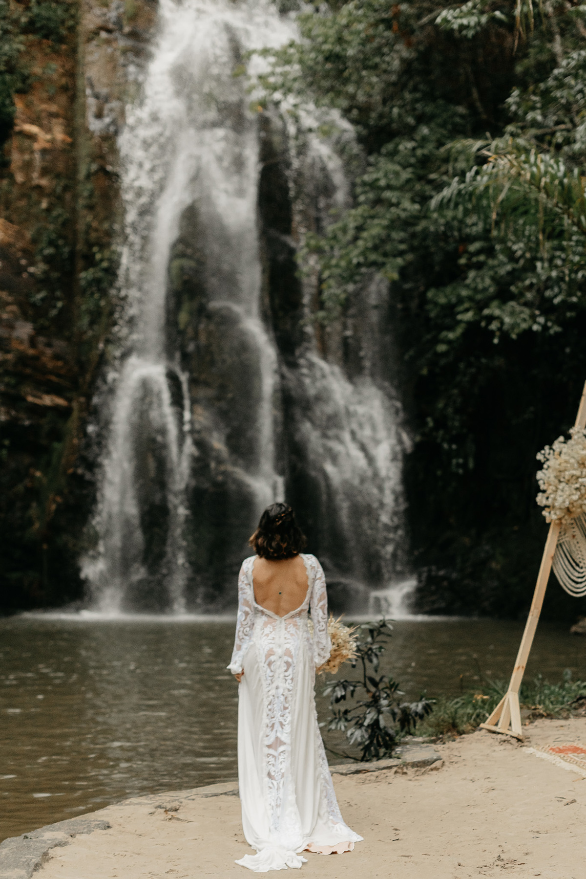 noiva com vestido boho de costas para a foto e de frente para a cachoeira, antes da chegada do noivo.