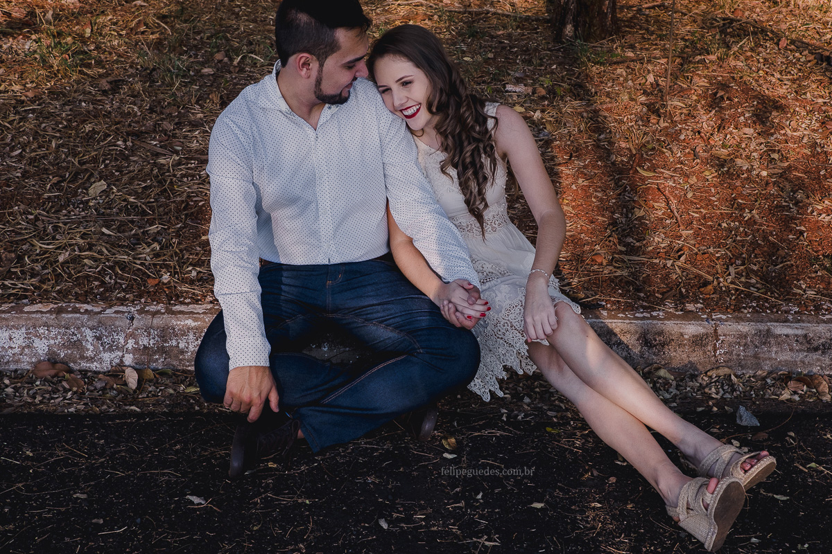 casal sentado no meio fio sorrindo em ensaio pre-wedding