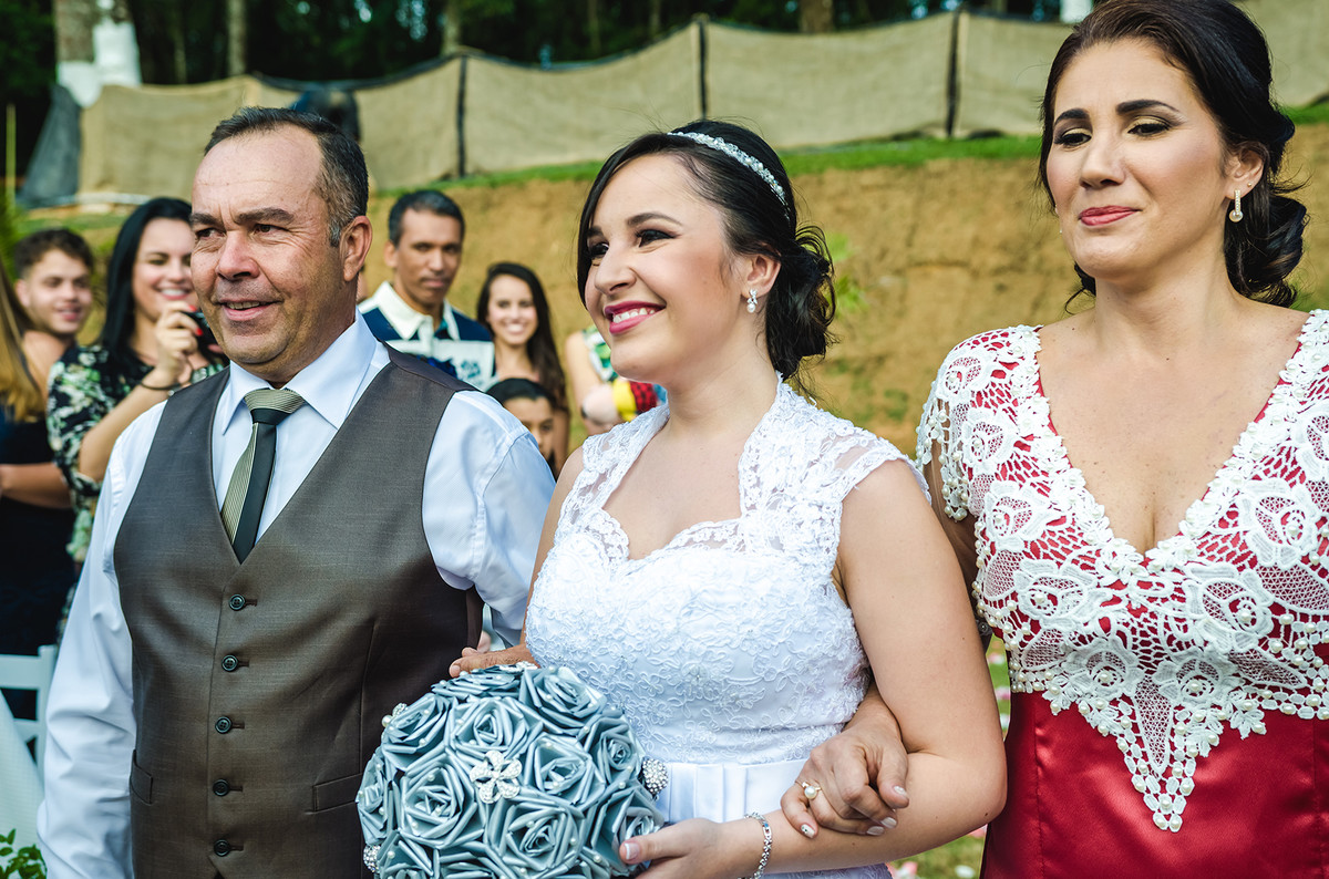 Fotografia de noiva entrando com o pai e a mãe em cerimônia de casamento 