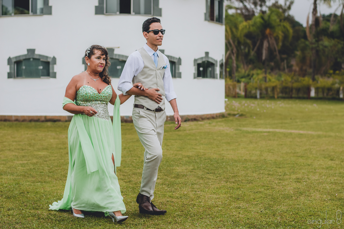 entrada-do-noivo-diferente-com-óculos-escuros-mae-do-noivo-de-verde-noivo-com-colete-e-calça-bege-casamento-de-dia-sitio-quatro-irmaos-fotografo-de-casamento-ibiuna-sao-paulo