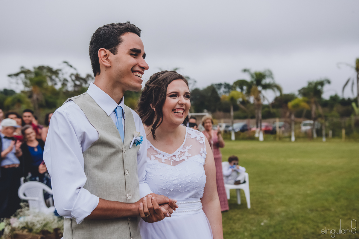 casal-feliz-após-cerimônia-evangélica-de-dia-sitio-quatro-irmãos-noivo-de-bege-noiva-com-trança-vestido-rendado