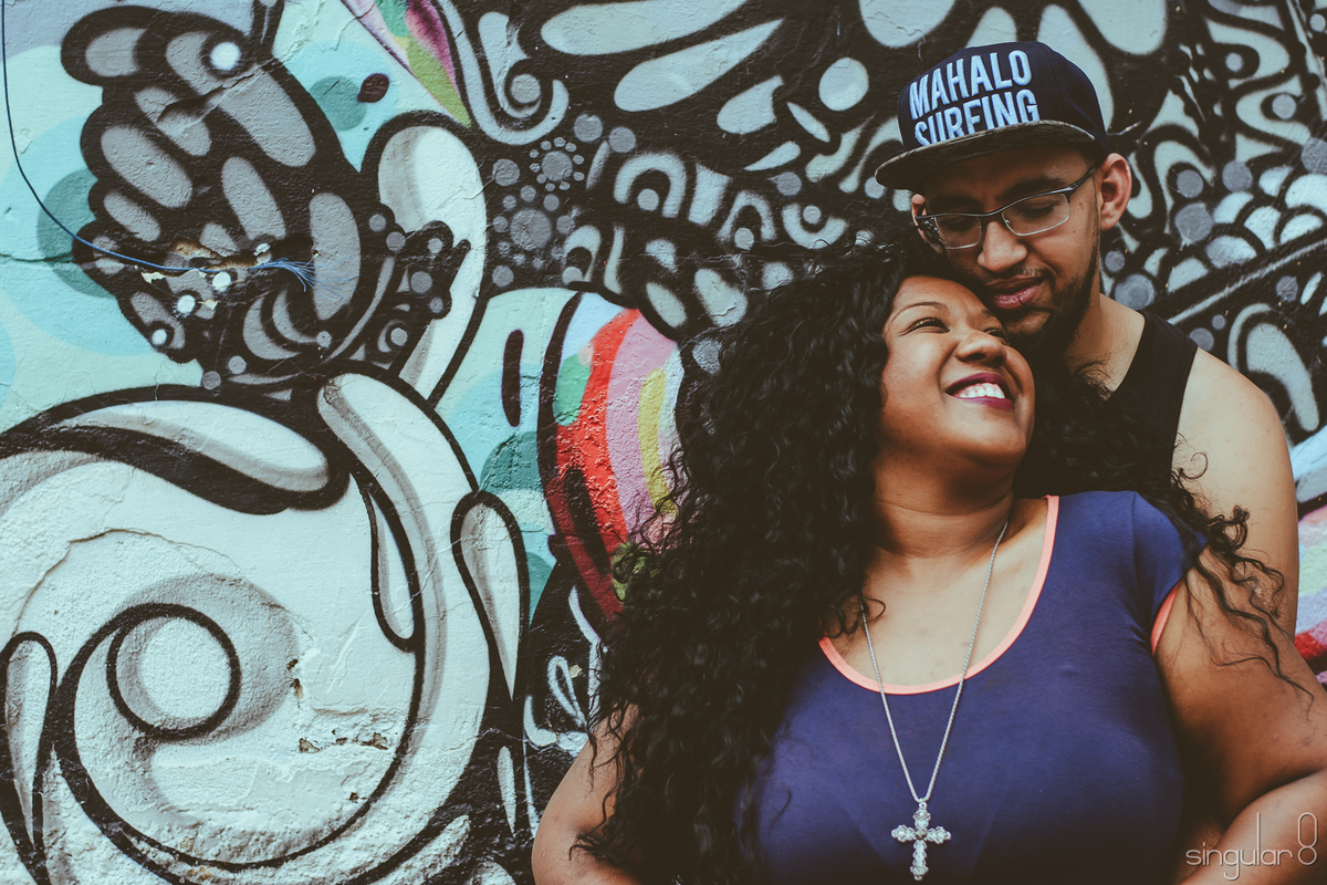Casal negro abraçados encostados na parede em ensaio fotográfico pré casamento no Beco do Batman