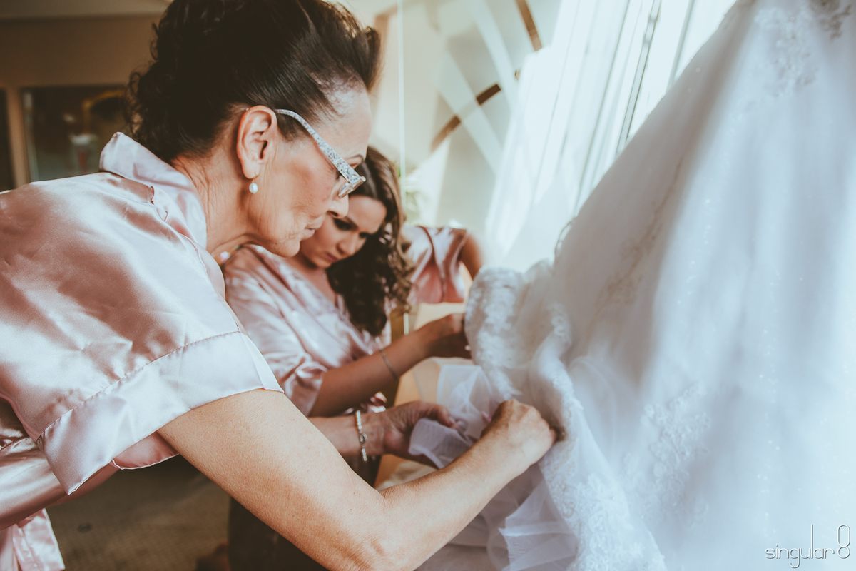 Mãe e madrinha pendurando os nomes das solteiras na barra do vestido da noiva