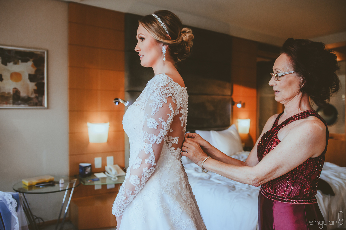 Fotografia da Mãe da noiva fechando os botões do vestido de casamento