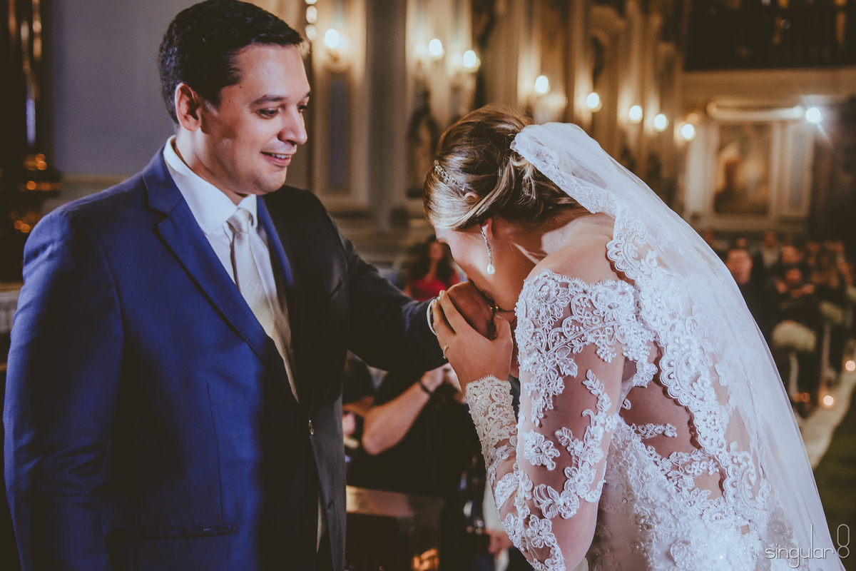 Noiva colocando as alianças e beijando a mão do noivo em cerimônia de casamento na Capela da Puc