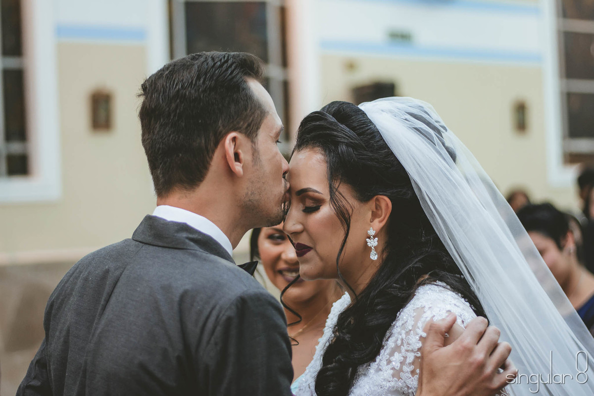 Foto do noivo beijando a testa da noiva na entrada da Igreja para cerimônia religiosa
