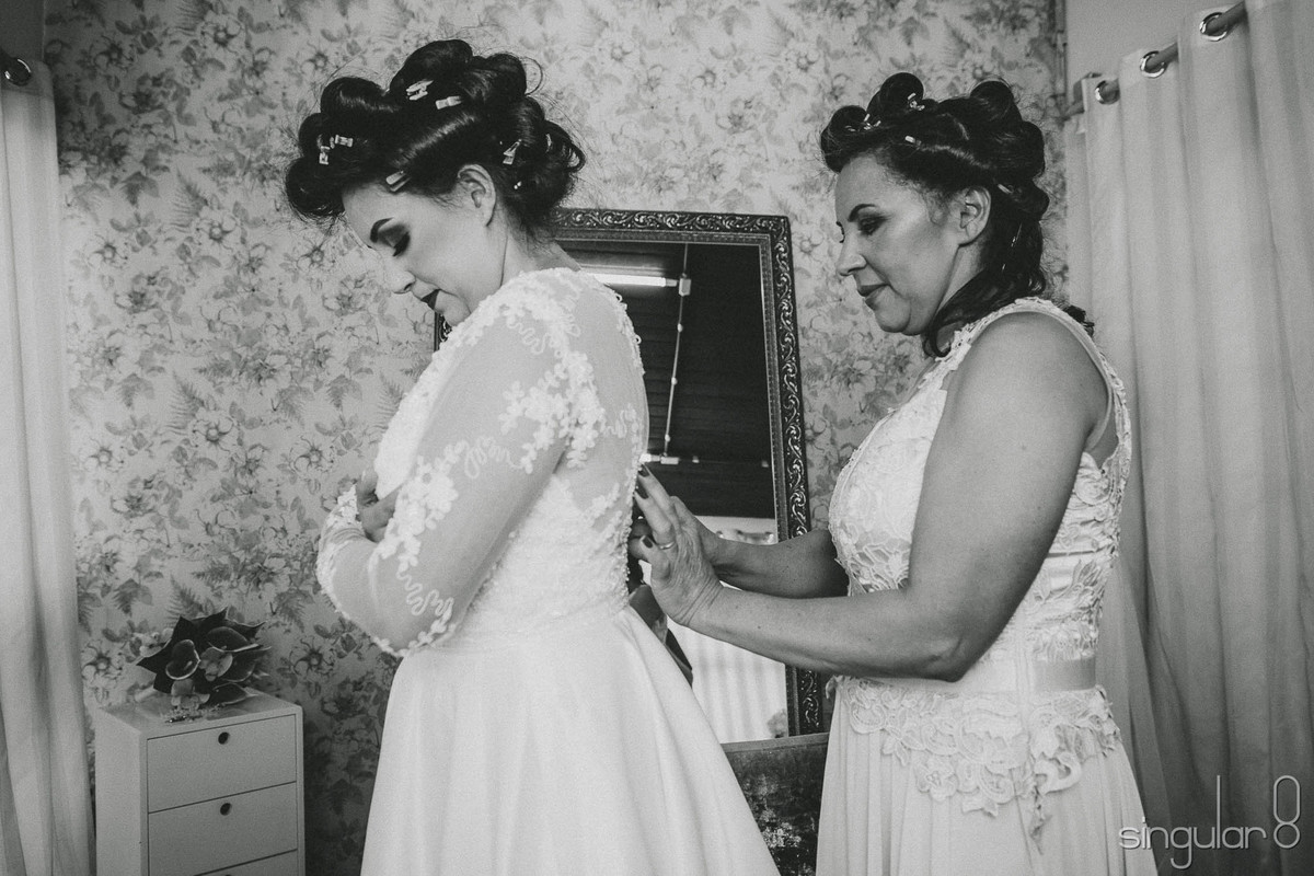 Fotografia da mãe fechando o vestido da noiva no making of no Studio Camila Toledo Mauá