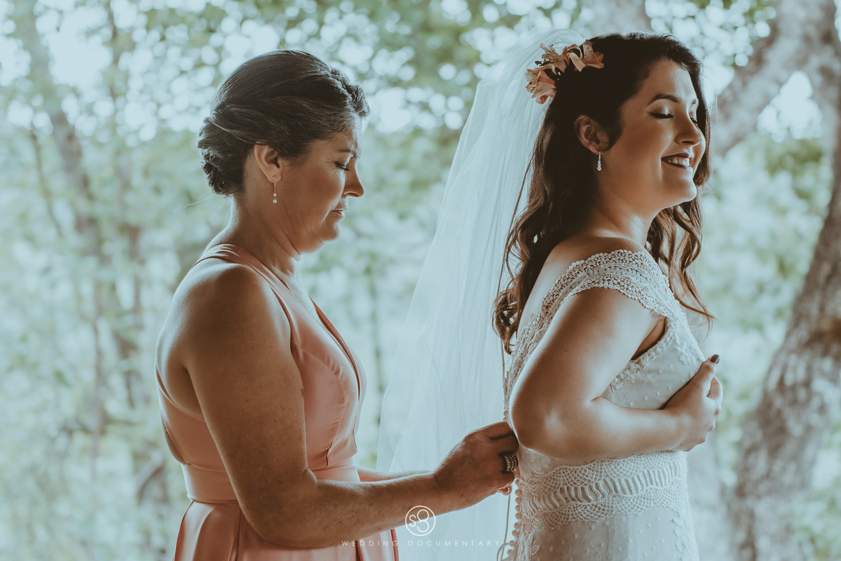Fotografia de casamento da mãe fechando o vestido de noiva