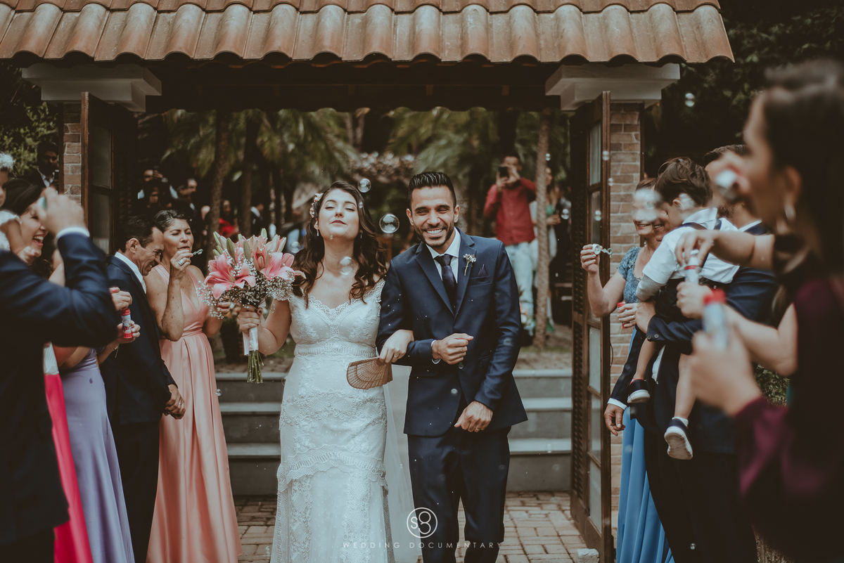 Fotografia de casamento da saída dos noivos com bolhas de sabão em casamento de Mairiporã