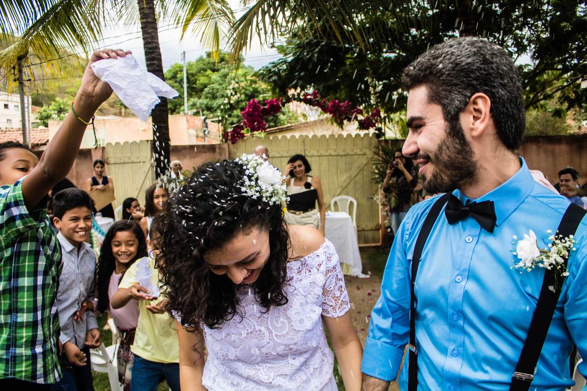 Fotografia de garoto virando saquinho de arroz na noiva durante a saída dos noivos em casamento realizado na cidade de Jampruca, Minas Gerais