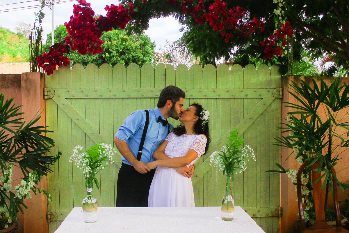 fotografia do beijo dos noivos próximo a portão de madeira e flores durante ensaio fotográfico pós casamento realizado na cidade de Jampruca Minas Gerais 