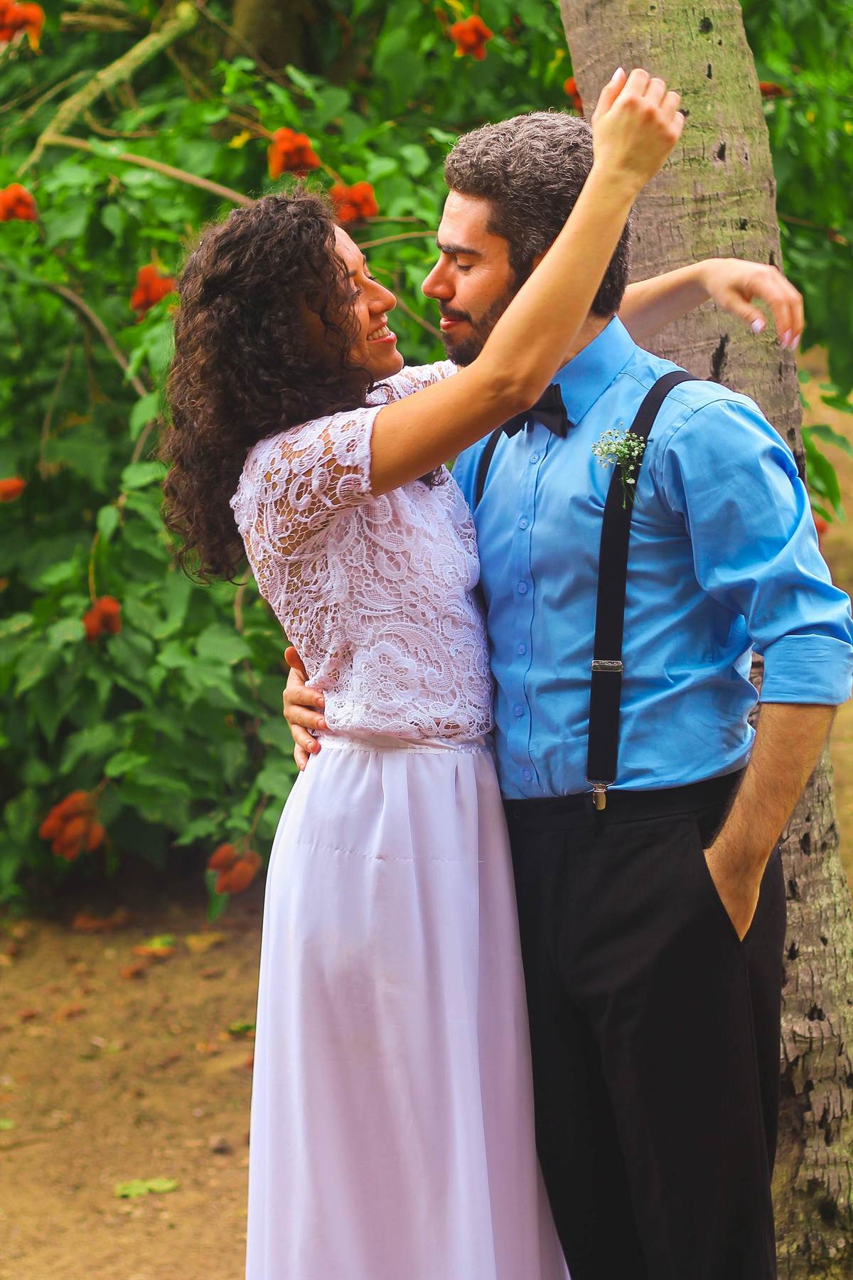 Fotografia dos noivos sorrindo abraçados se olhando, próximo a árvore de urucu durante ensaio fotográfico pós casamento realizado na cidade de Jampruca Minas Gerais 