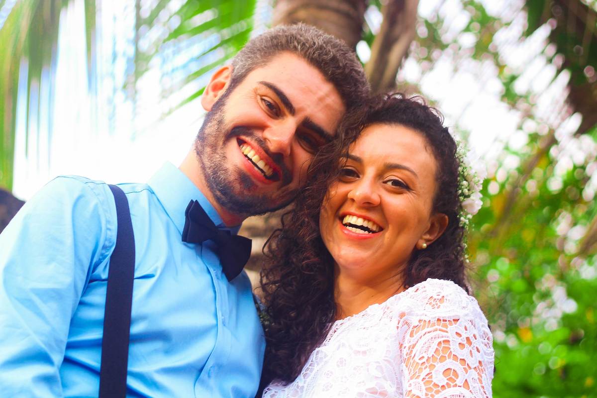 Fotografia dos noivos sorrindo, próximo a coqueiro durante ensaio fotográfico pós casamento realizado na cidade de Jampruca Minas Gerais 
