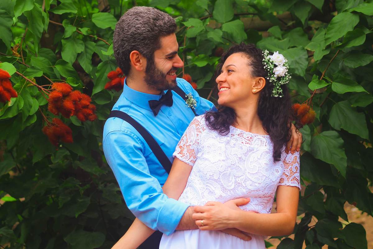 Fotografia dos noivos sorrindo abraçados se olhando, próximo a árvore de urucu durante ensaio fotográfico pós casamento realizado na cidade de Jampruca Minas Gerais 