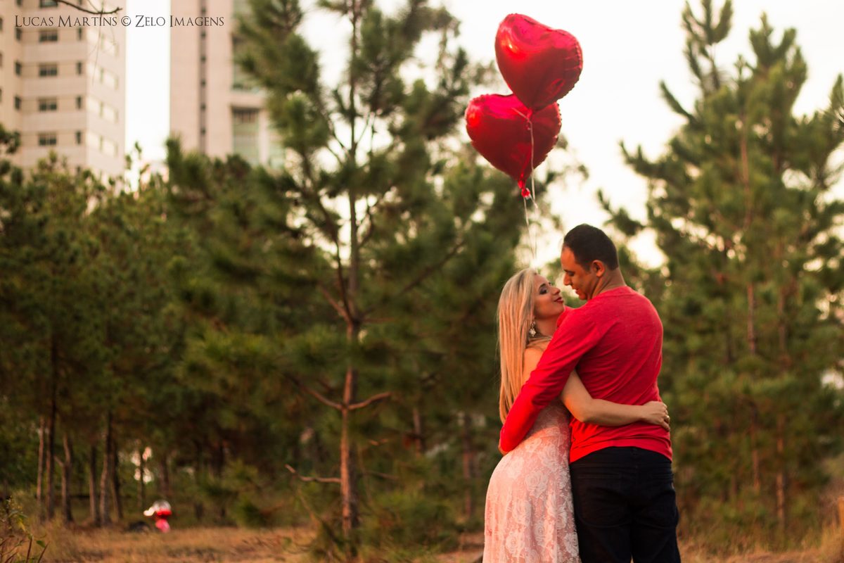 Fotografia dos noivos segurando balões de coração, perto de arvores, nos trilhos antigos do Belvedere em Belo Horizonte