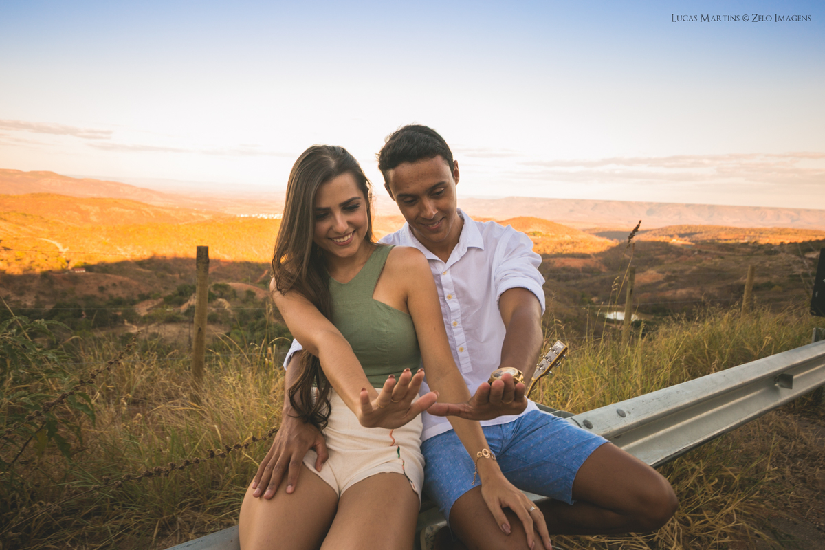 casal sentados no alambrado da rodovia olhando as maos com as aliancas