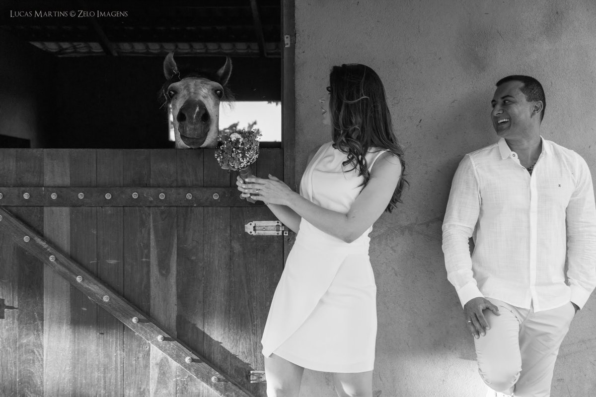 casal posando junto ao um cavalo a noiva chegando o bouquet proximo do cavalo