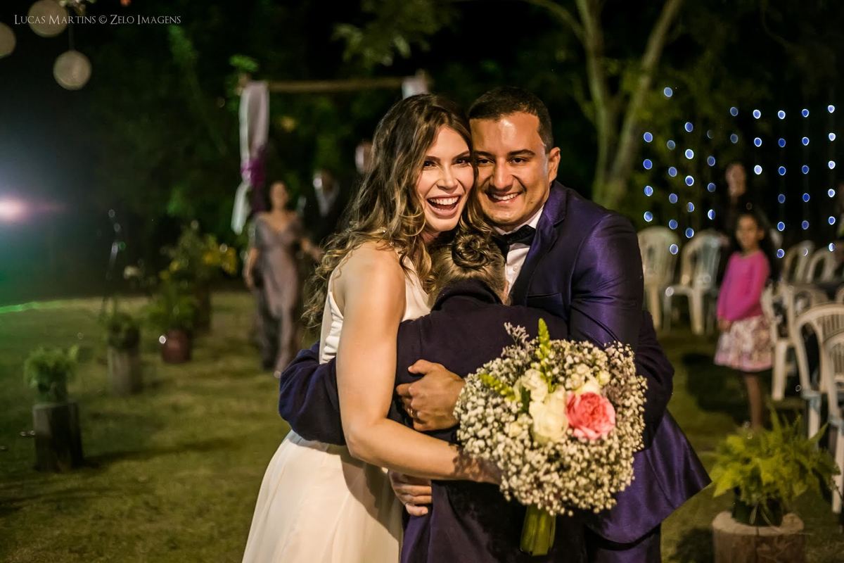 noivos abracando convidada com buque na mao