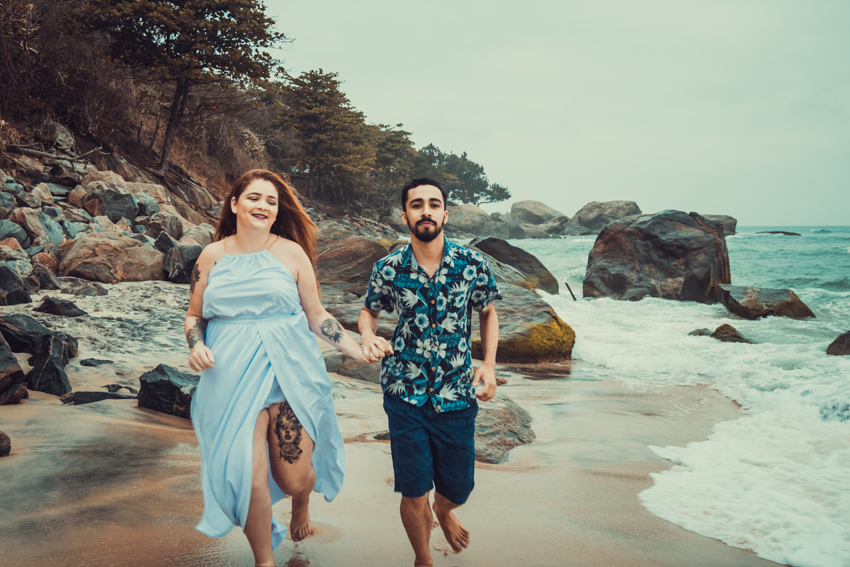 fotografia do casal correndo na faixa de areia próximo ao mar, durante ensaio fotográfico de casal na praia de Grumari, Rio de Janeiro - RJ