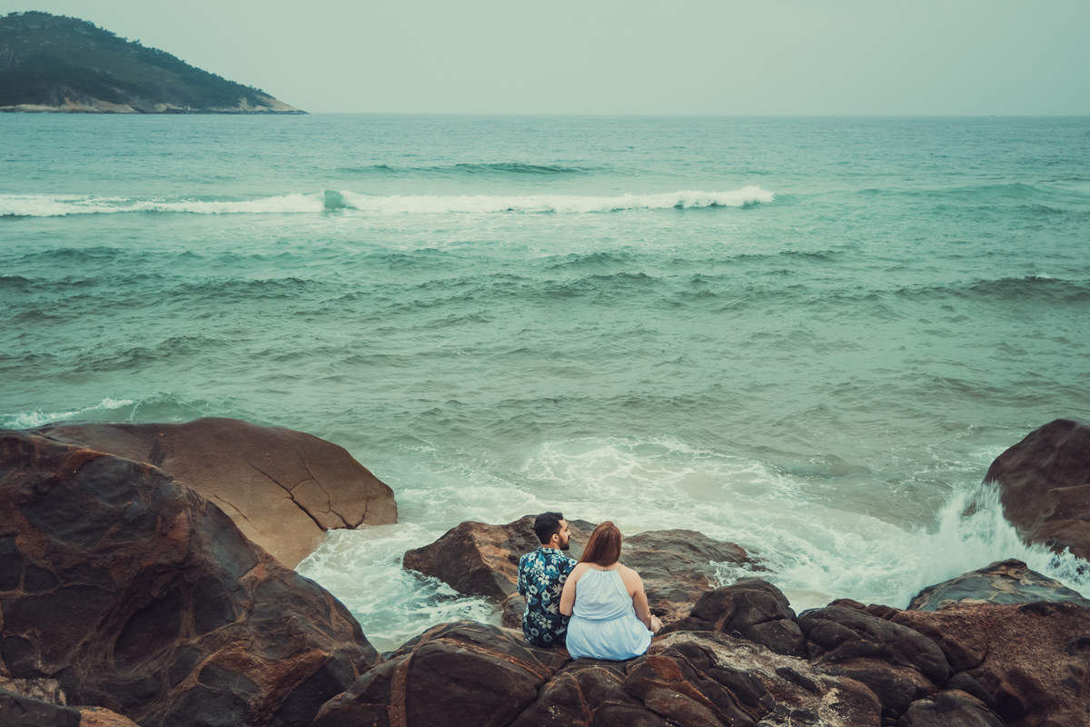 fotografia de casal sentado nas pedras admirando o mar no fim de tarde durante ensaio fotográfico na praia de Grumari, Rio de Janeiro, RJ
