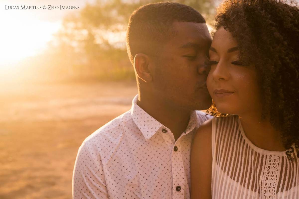fotografia de rapaz dando um beijo no rosto da namorada, ambos de olhos fechados, durante por do sol em ensaio fotográfico de casal em Araçuaí - MG