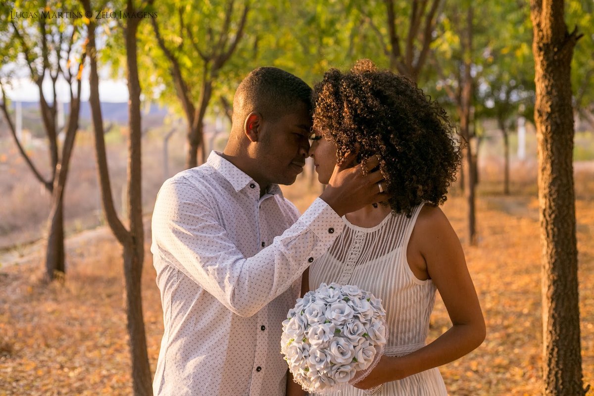 Fotografia de casal encostando testa com testa, com buquê de flores, entre as arvores em  ensaio fotográfico de casal realizado em Araçuaí - MG