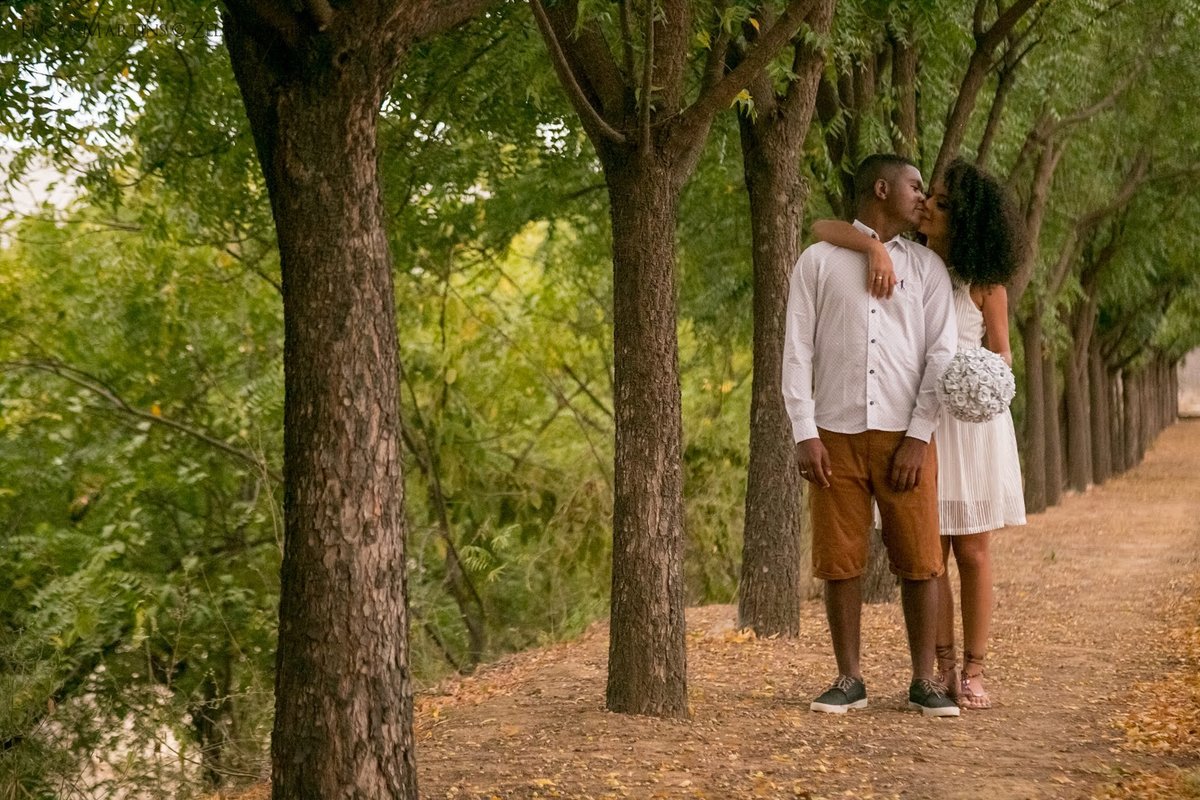 fotografia de casal se beijando com buquê de flores em um caminho de árvores, durante ensaio fotográfico de casal realizado em Araçuaí, Minas Gerais