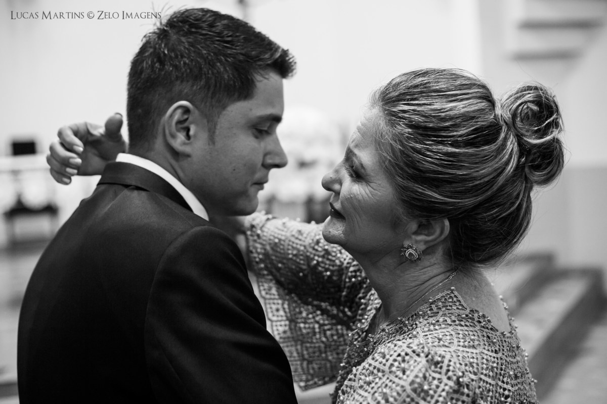 fotografia da mãe do noivo abraçando-o ao deixá-lo no altar durante a cerimônia de casamento.