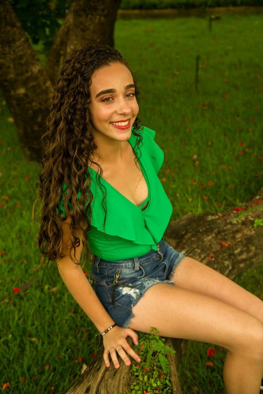 debutante posando para a foto sentada em um troco de arvore em um campo gramado