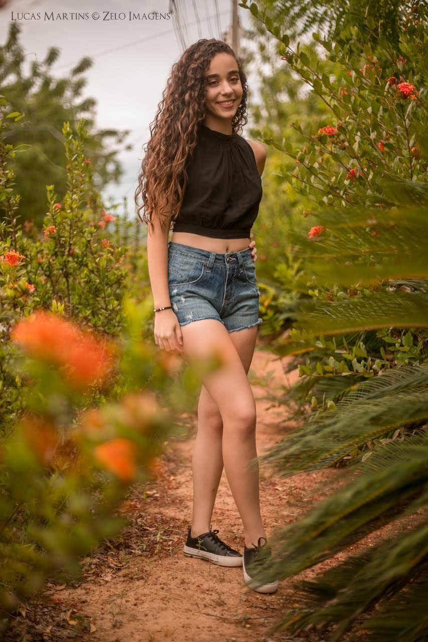 Debutante sorrindo em um campo de flores em ensaio 15 anos feito na cidade de Araçuai, Minas Gerais