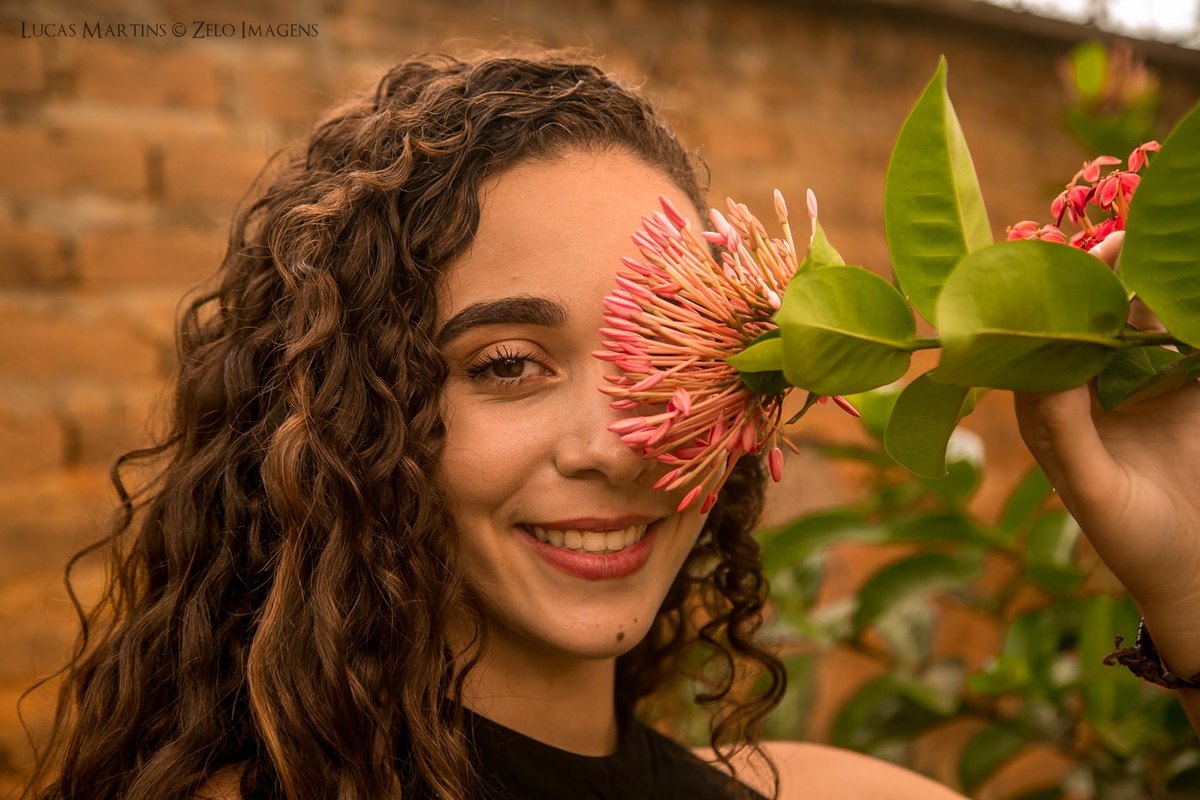 Debutante sorrindo segurando uma flor perto do rosto