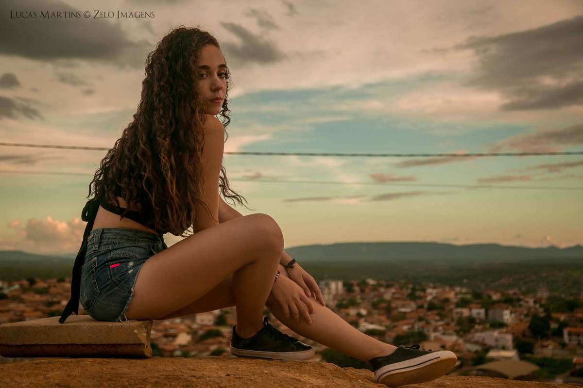 debutante posando para a foto sentada no chão com a cidade ao fundo