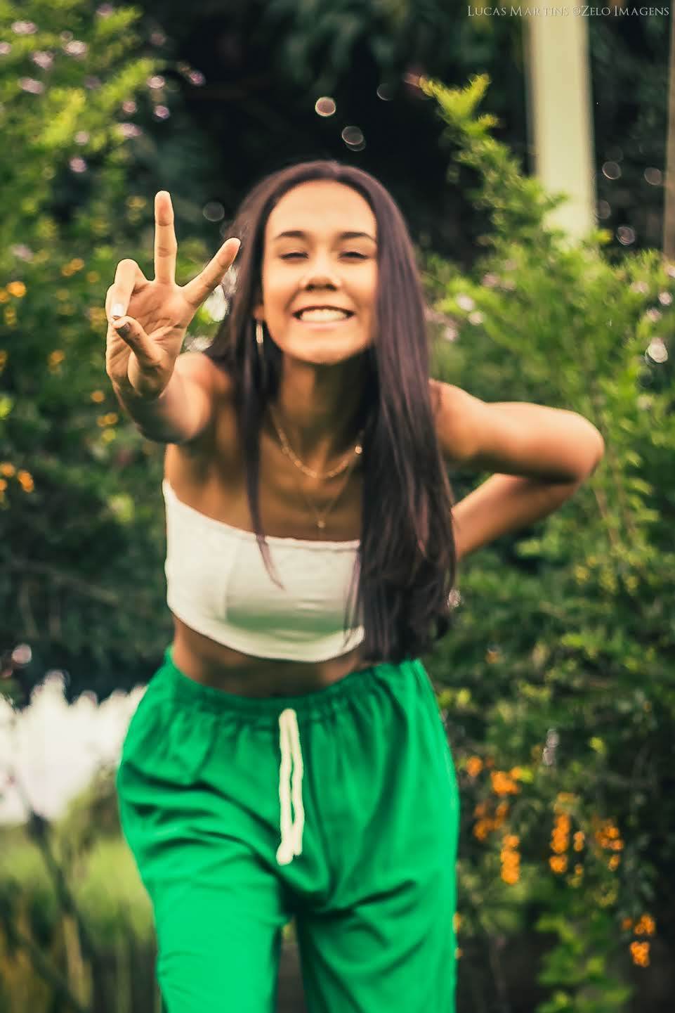 Fotografia da debutante fazendo simbolo de paz e amor com a mão e sorrindo durante  ensaio fotográfico de 15 anos em Virgem da Lapa - mg