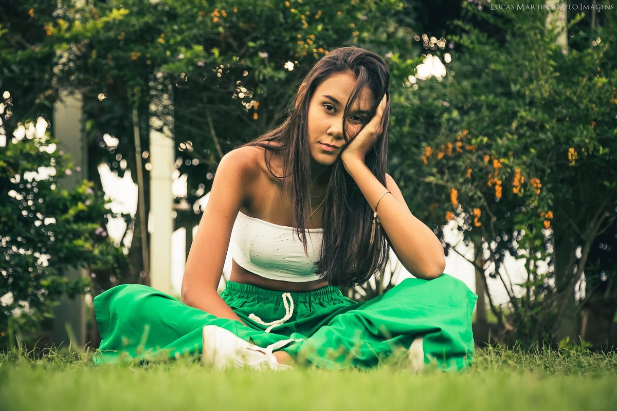 fotografia da debutante sentada na grama com mão no rosto durante ensaio fotográfico 15 anos na cidade de Virgem da Lapa, Minas Gerais