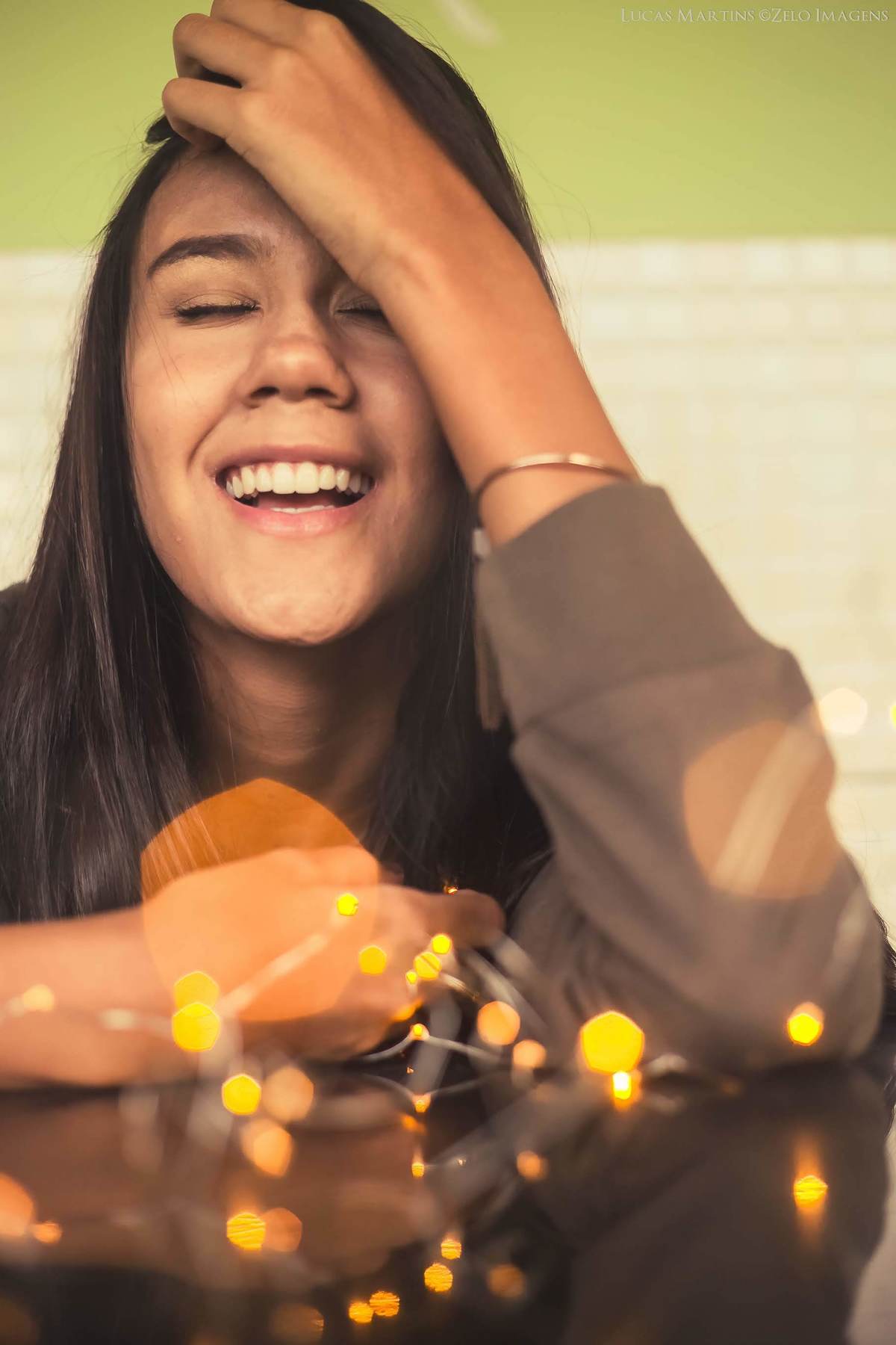 Fotografia de debutante sorrindo, com luzes, fio de fada, durante ensaio fotográfico 15 anos em Virgem da Lapa, Minas Gerais.