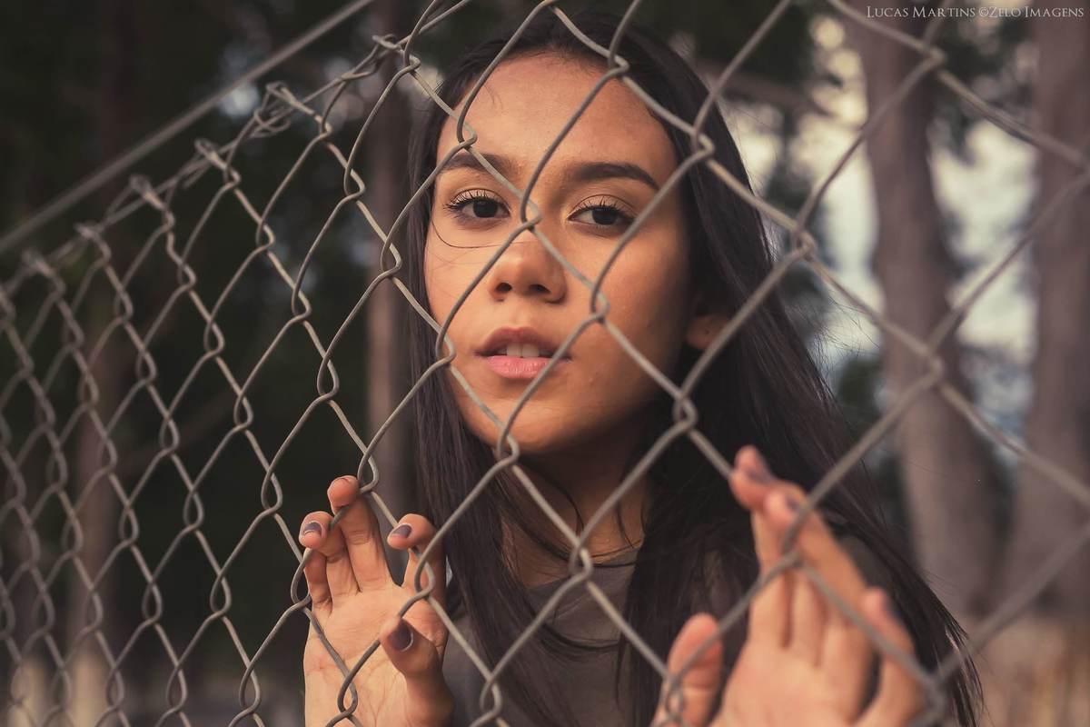 ensaio fotográfico 15 anos. Debutante faz pose segurando em cerca de grade, em Virgem da Lapa, Minas Gera