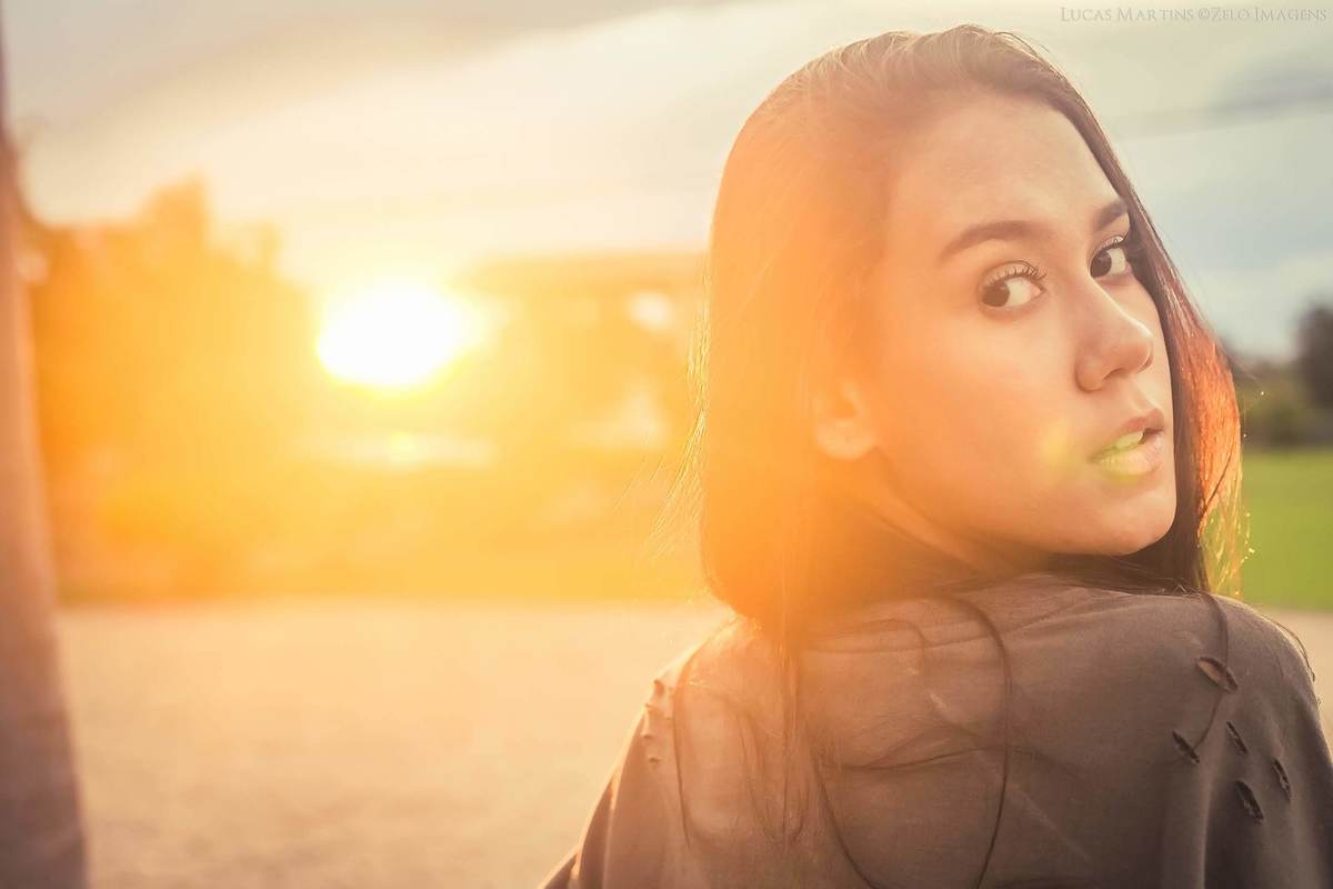 foto da debutante de costas olhando para a câmera com por do sol ao fundo, durante ensaio fotográfico de 15 anos feito na cidade de Virgem da Lapa, Minas Gerais.