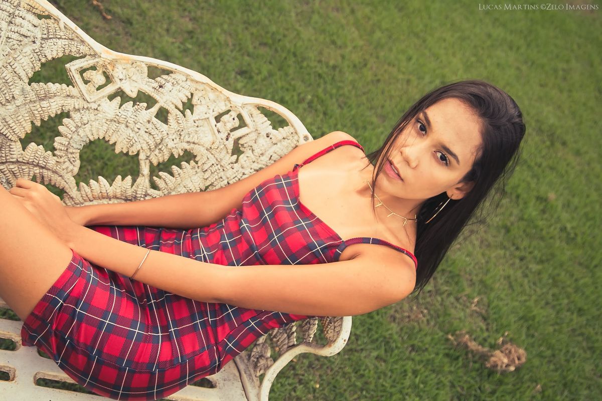 fotografia de debutante sentada em banco em gramado olhando para a câmera em ensaio fotográfico 15 anos feito na cidade de Virgem da Lapa, Minas Gerais