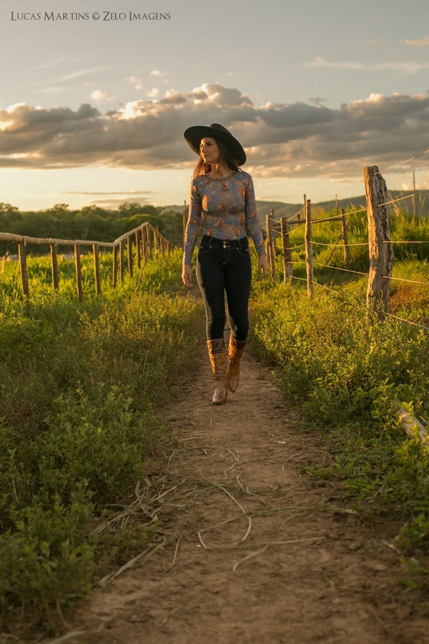 Foto da debutante andando em caminho entre as cercas durante ensaio fotográfico 15 anos realizado na cidade de Araçuaí, Minas Gerais