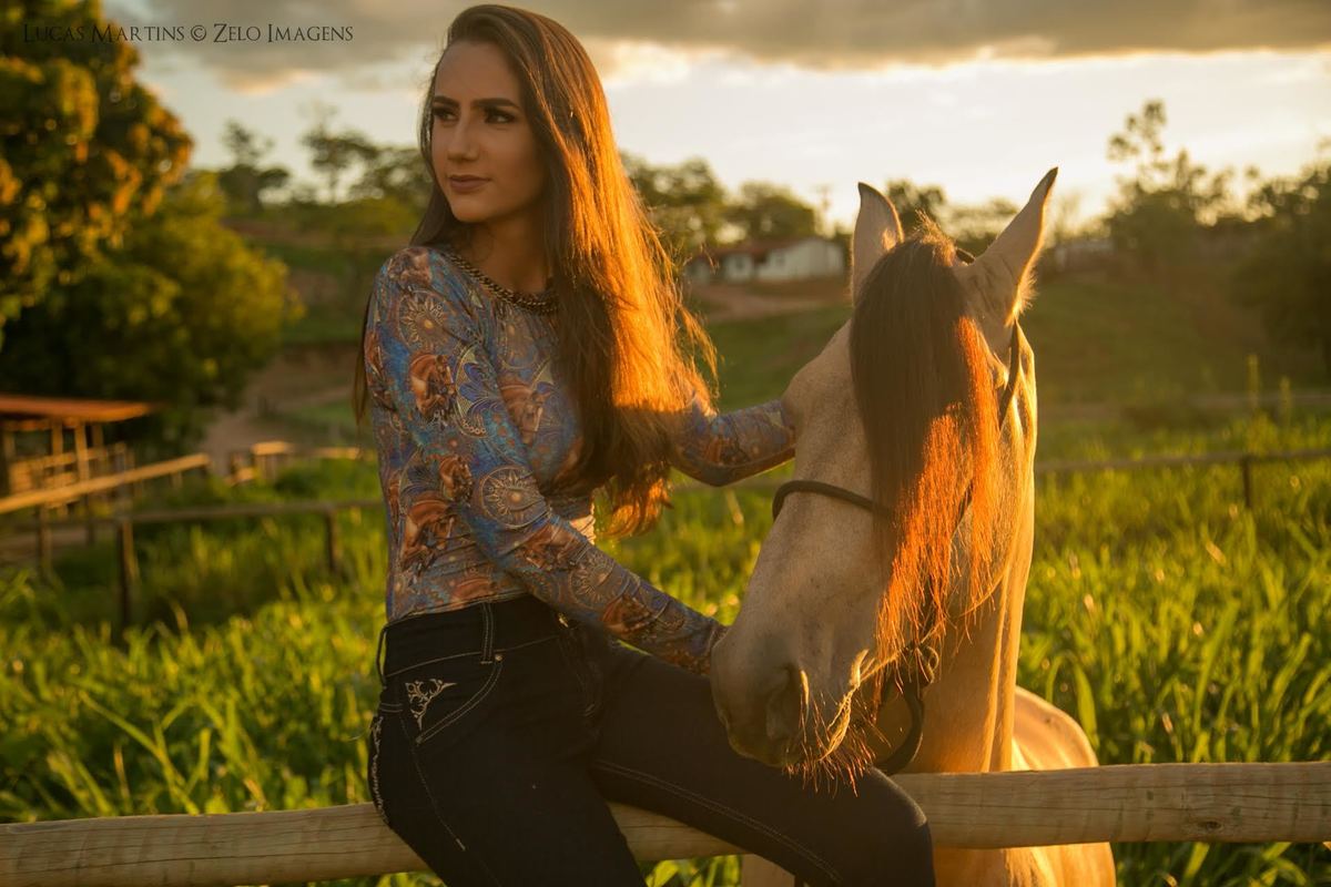 fotografia da debutante sentada em cima da cerca, junto ao cavalo, ambos olhando para a mesma direção, em ensaio fotográfico 15 anos feito na cidade de Araçuaí - MG